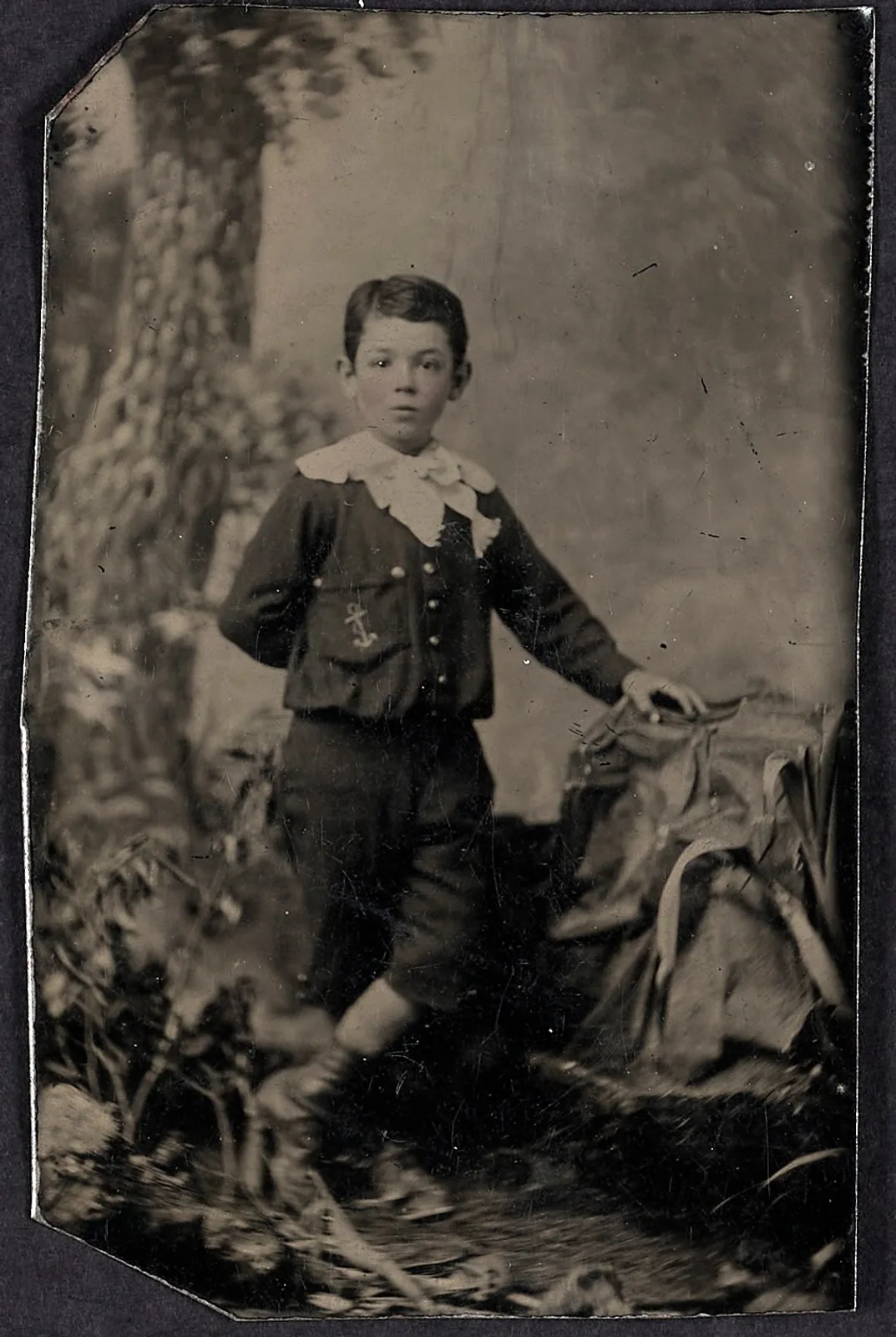Original: A boy in a buttoned jacket and lace collar beside a studio prop, tintype