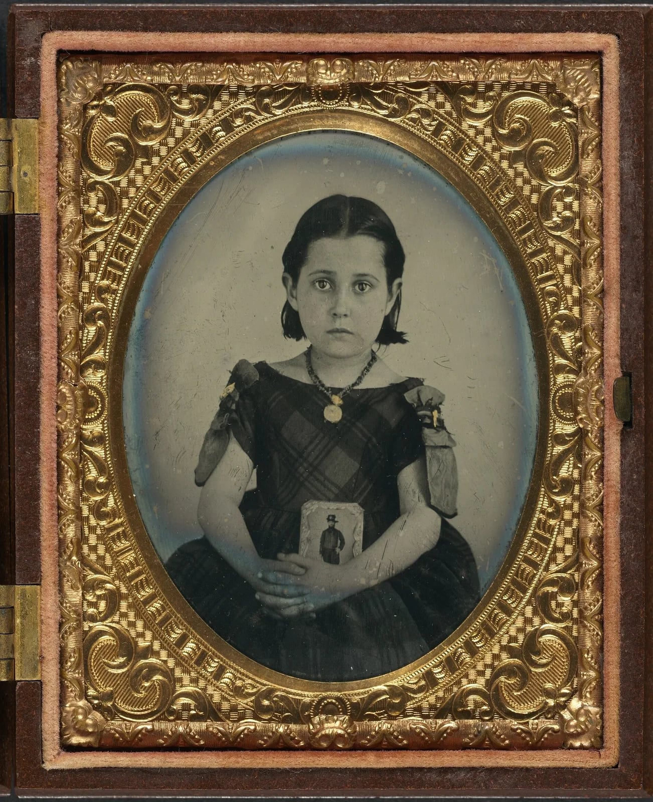 Original: A girl in a plaid dress holding a small framed photograph, in a gilt case